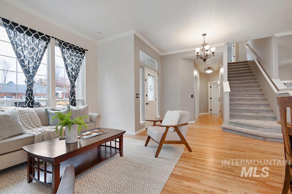 Living room with stairway, healthy amount of natural light, light wood-style flooring, ornamental molding, and a chandelier