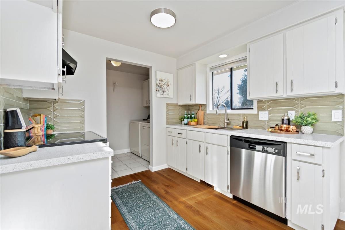 Kitchen featuring stainless steel dishwasher, tasteful backsplash, white cabinets, and washing machine and dryer