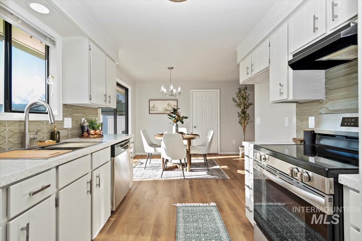 Kitchen with backsplash, stainless steel appliances, extractor fan, white cabinets, and a chandelier