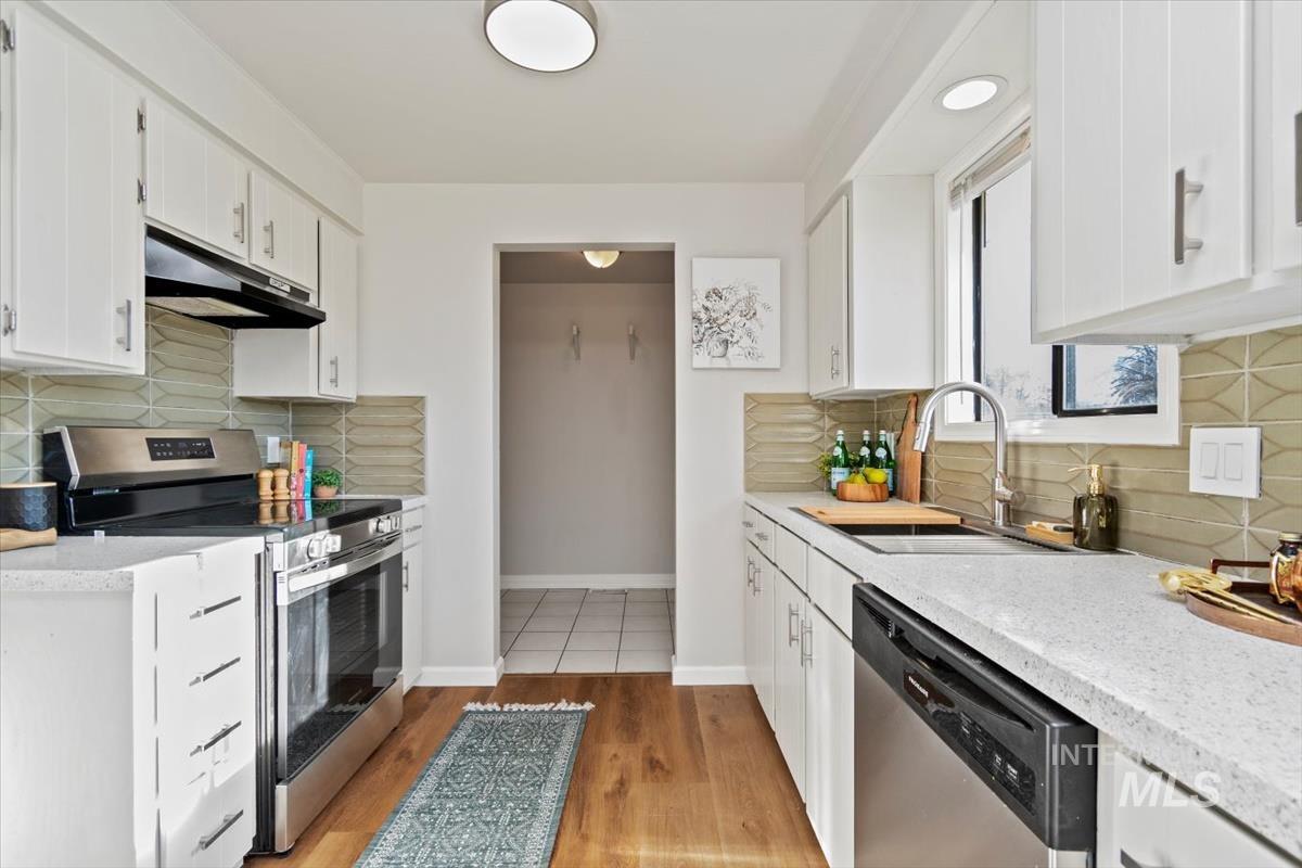 Kitchen with stainless steel appliances, white cabinetry, under cabinet range hood, and light wood finished floors