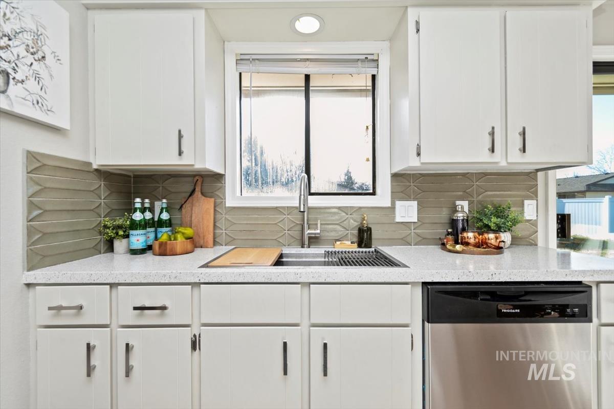 Kitchen with stainless steel dishwasher, white cabinets, light stone counters, and backsplash