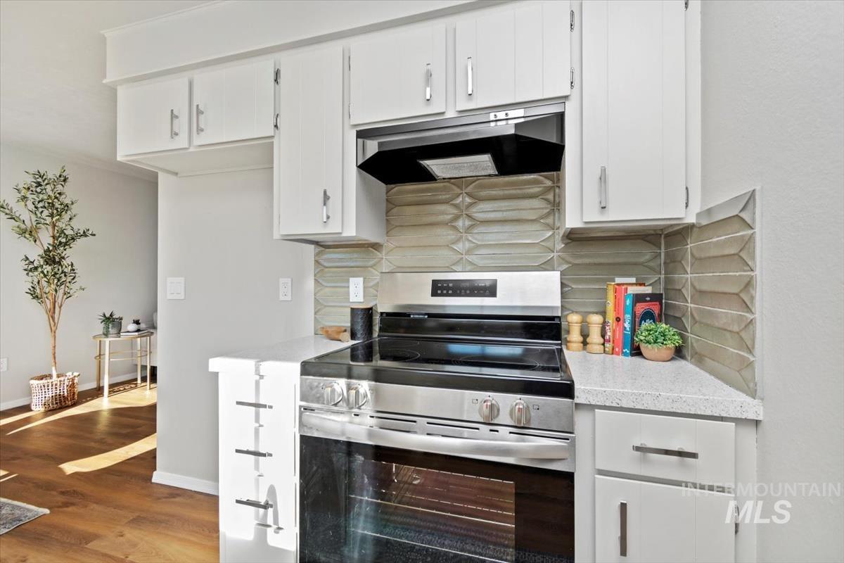 Kitchen with stainless steel range with electric cooktop, tasteful backsplash, white cabinetry, under cabinet range hood, and dark wood-style flooring
