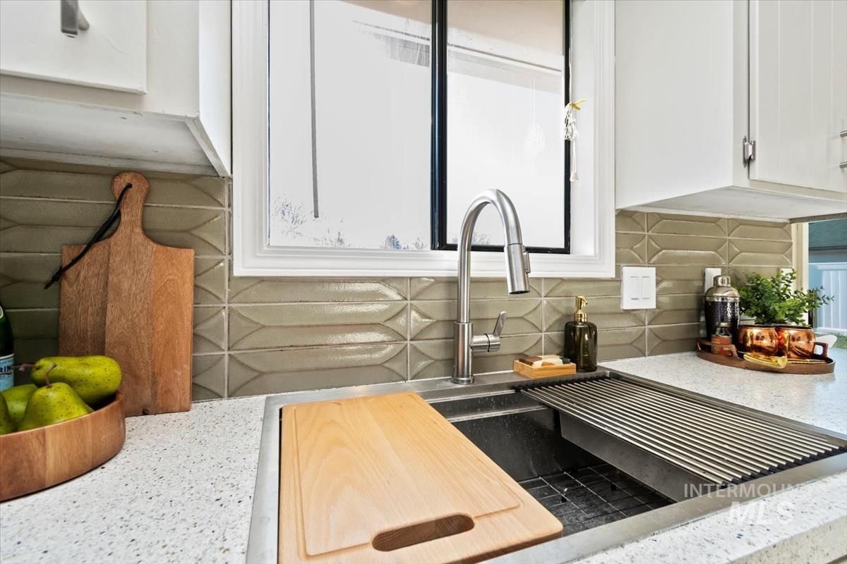Kitchen featuring white cabinets, light stone counters, and backsplash