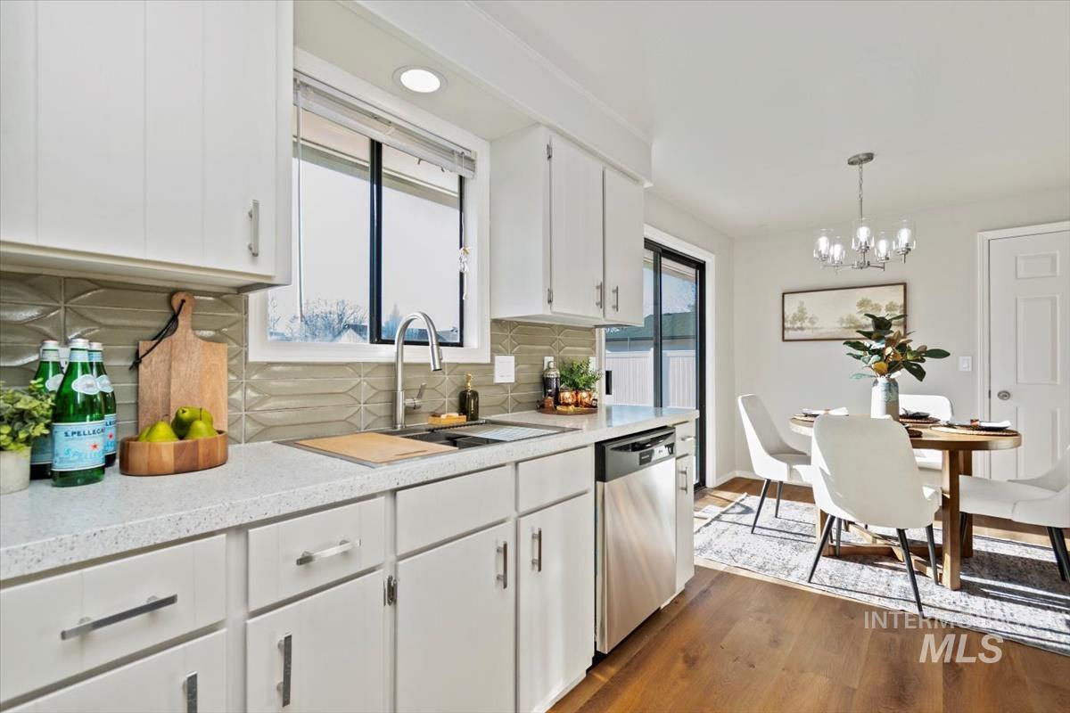 Kitchen with decorative backsplash, white cabinetry, dishwasher, dark wood-type flooring, and a chandelier