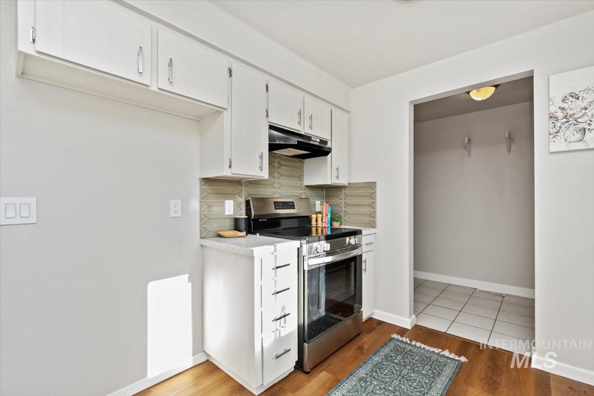 Kitchen featuring stainless steel electric range oven, light countertops, tasteful backsplash, white cabinets, and light wood-style flooring