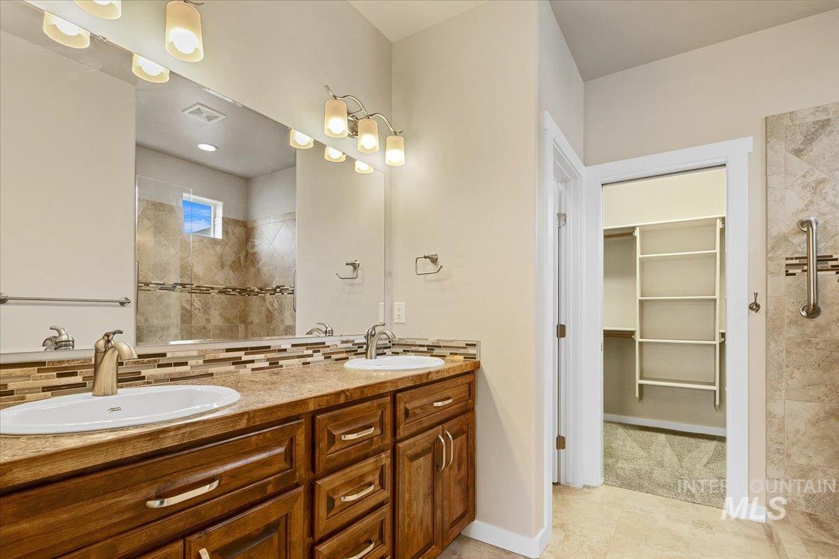 Bathroom featuring double vanity, walk in shower, a spacious closet, and backsplash. Heated Flooring
