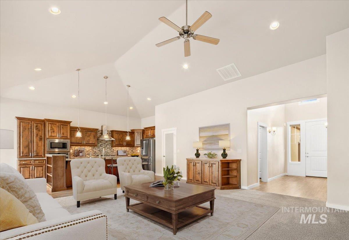 Living room with high vaulted ceiling, ceiling fan, new light carpet, and recessed lighting