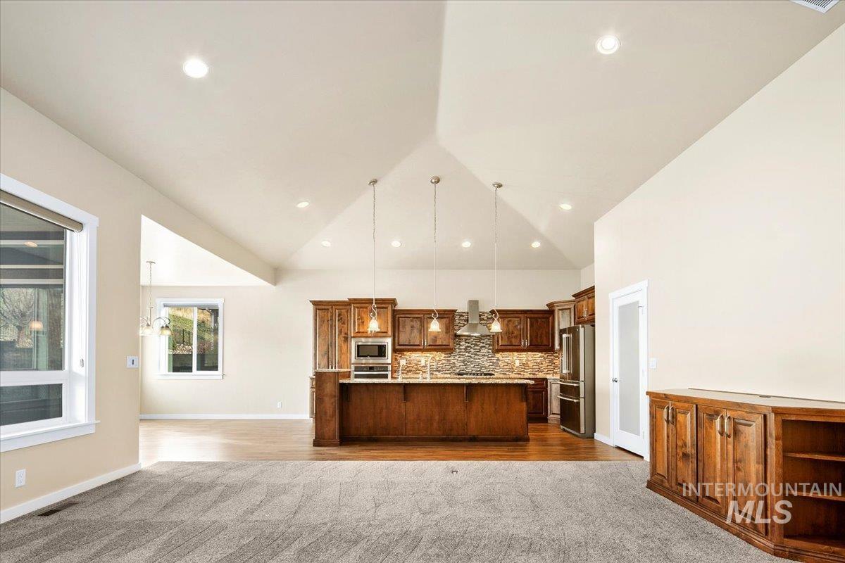 Kitchen with decorative light fixtures, a spacious island, open floor plan, stainless steel appliances, and dark wood-type flooring