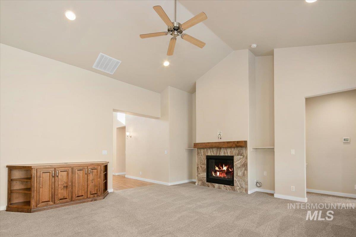 Unfurnished living room featuring high vaulted ceiling, a tiled fireplace, light colored carpet, ceiling fan, and recessed lighting