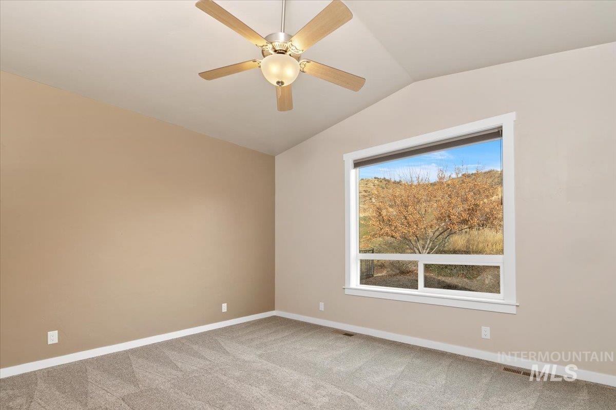 Empty room with lofted ceiling, carpet flooring, and ceiling fan