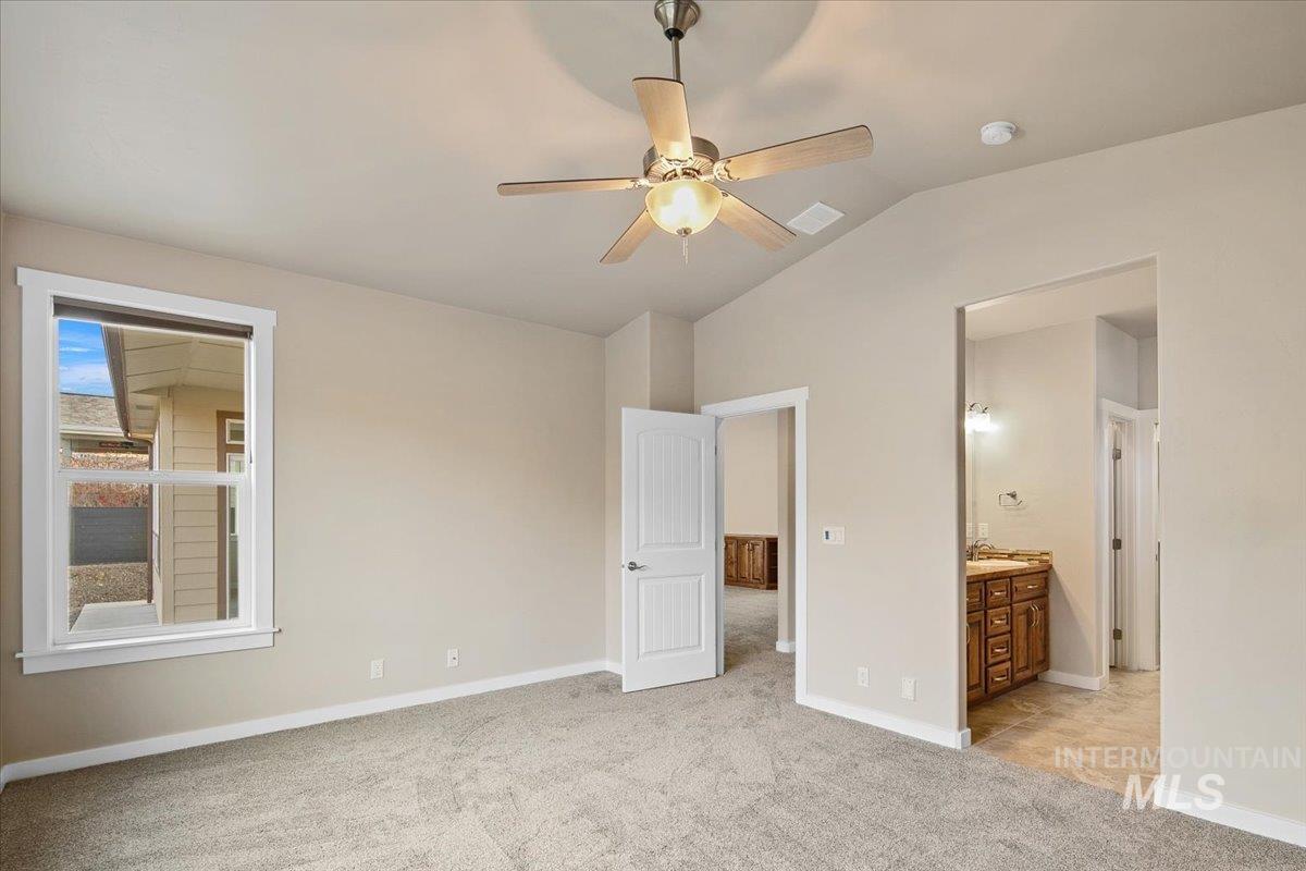 Unfurnished bedroom featuring light carpet, lofted ceiling, a ceiling fan, and connected bathroom