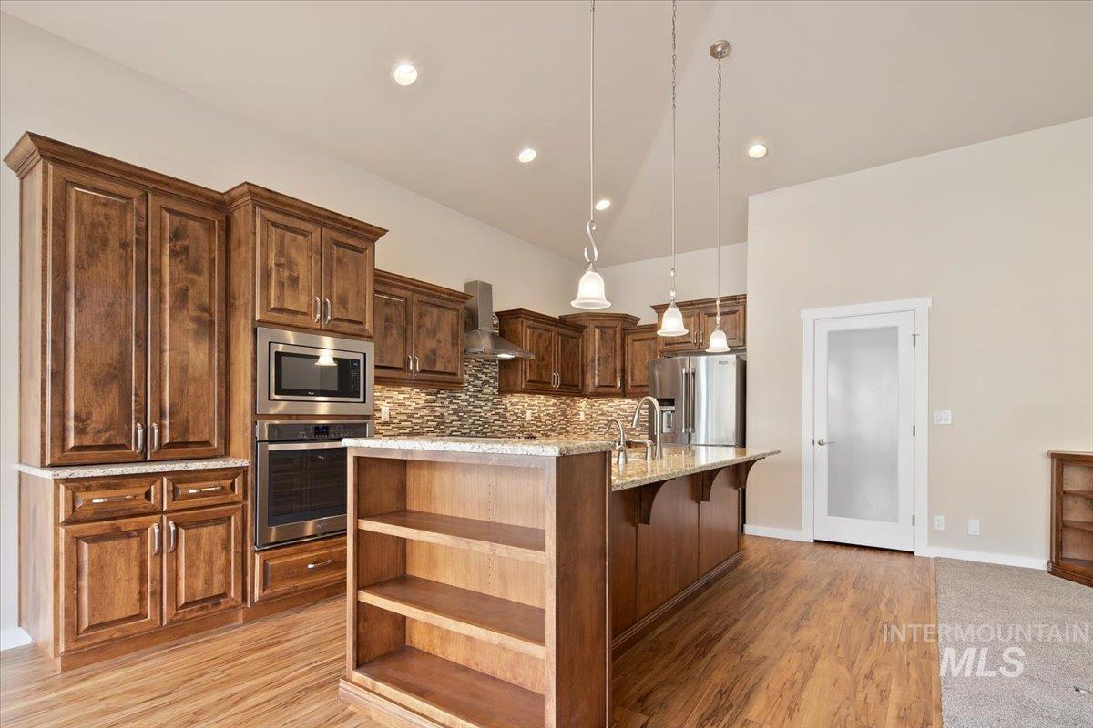 Kitchen featuring open shelves, an island with sink, pendant lighting, stainless steel appliances, and a breakfast bar