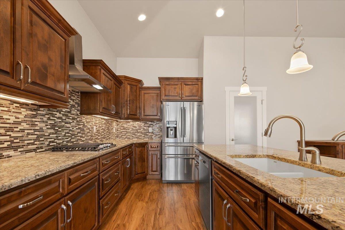 Kitchen featuring appliances with stainless steel finishes, hanging light fixtures, wall chimney range hood, light stone counters, and recessed lighting