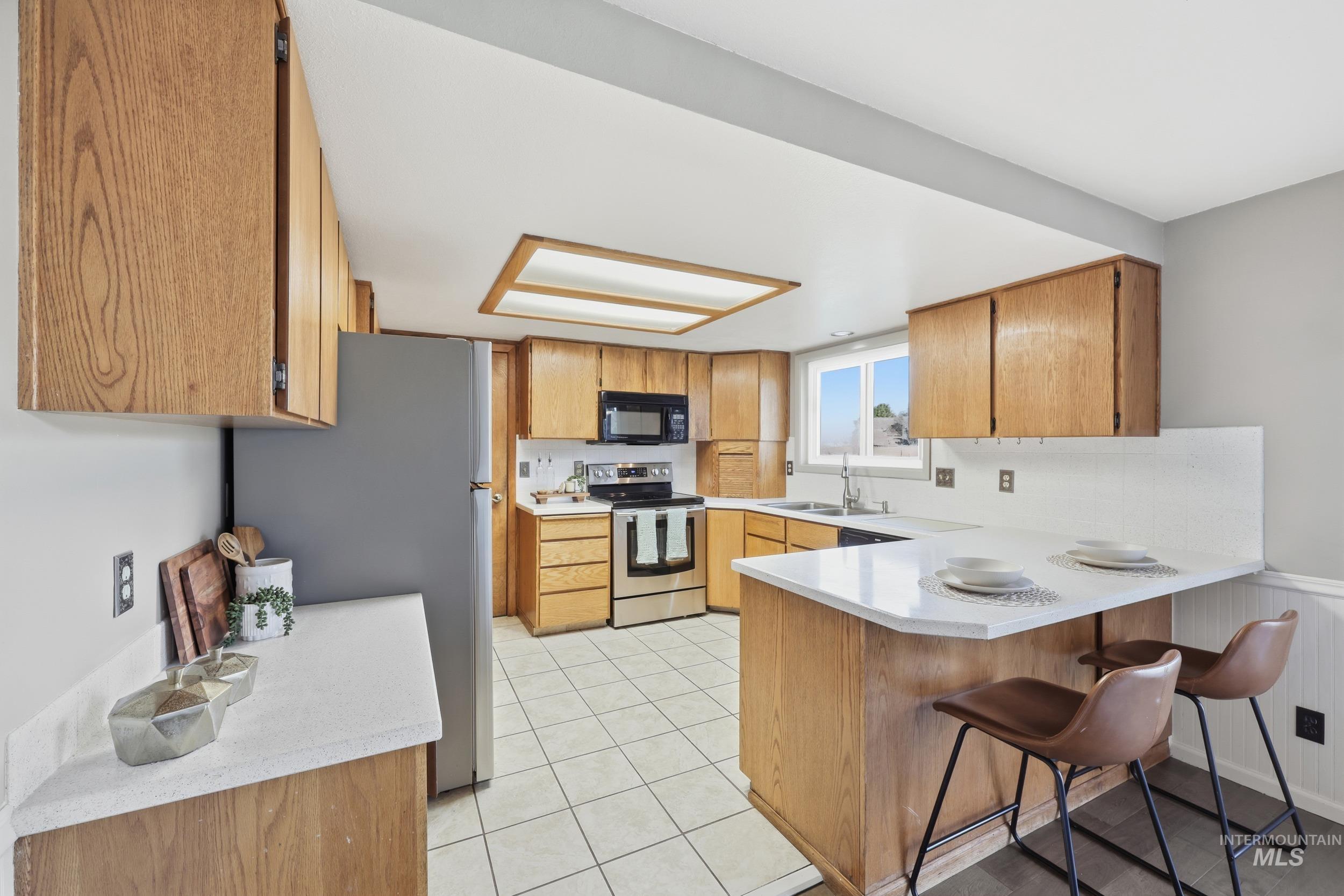 Kitchen featuring a peninsula, light countertops, appliances with stainless steel finishes, and a kitchen bar