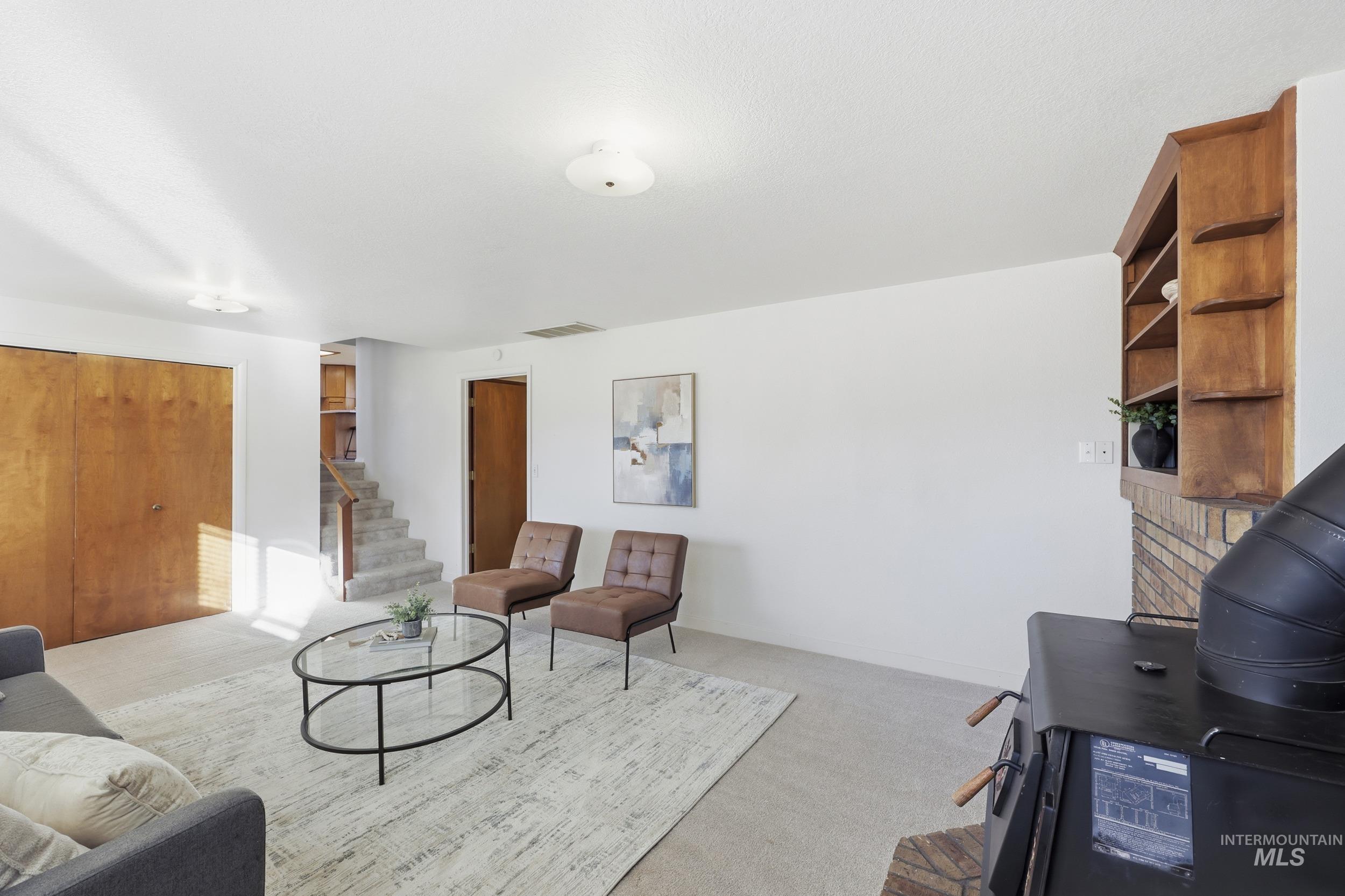Newly carpeted living area with stairs and large storage closets and a wood stove.