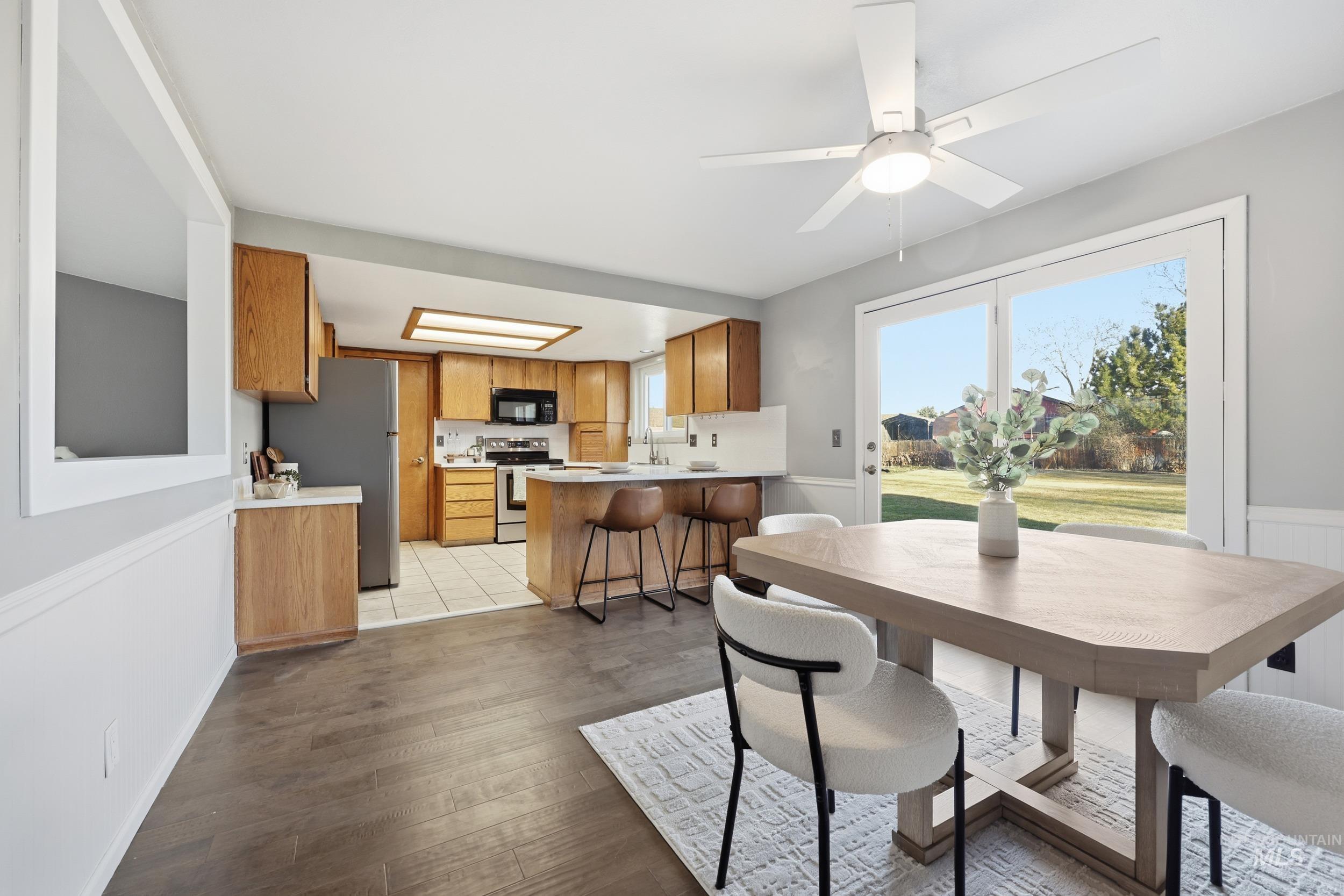 Dining space featuring new engineered hardwood flooring, a ceiling fan, and a wainscoted accent wall.