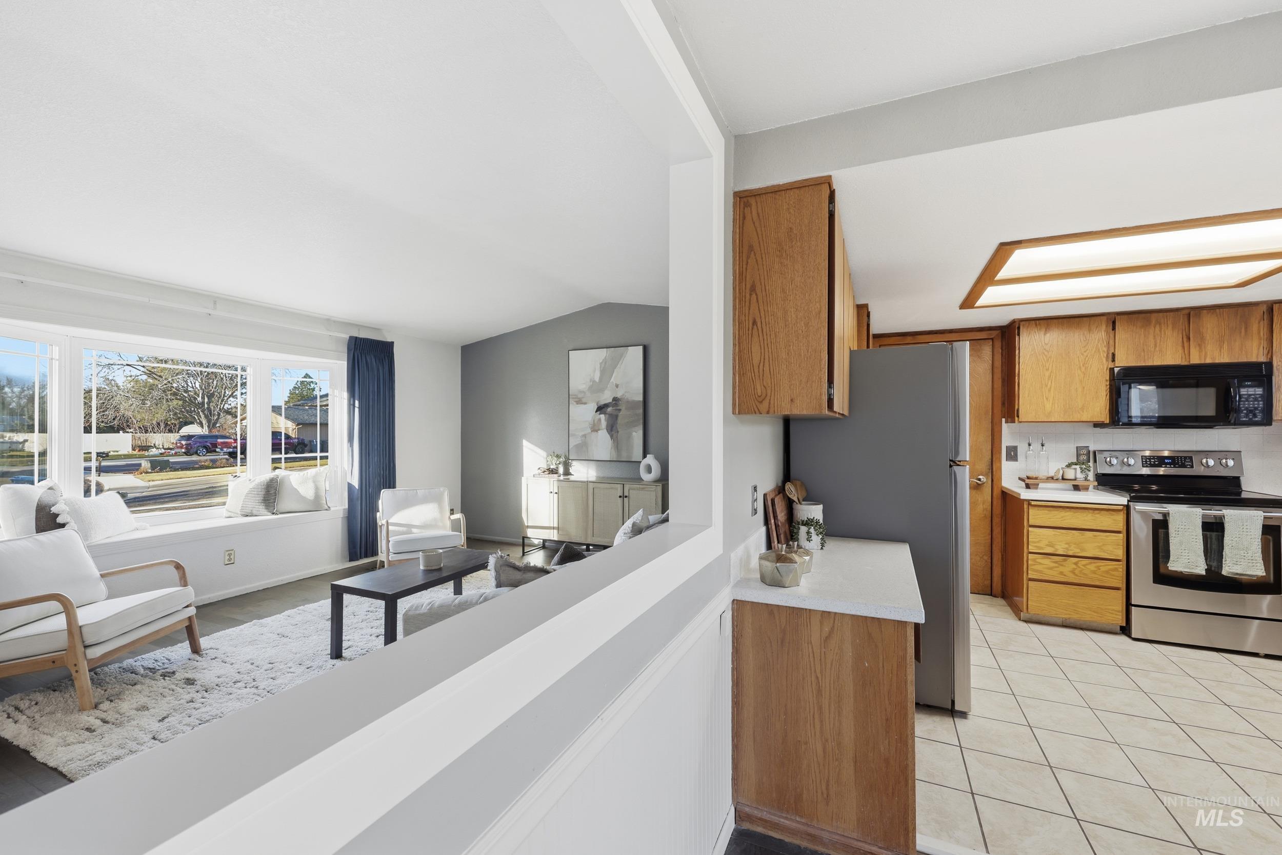 Kitchen featuring open view into the living room, light hardsurface countertops, appliances, and vaulted ceiling.