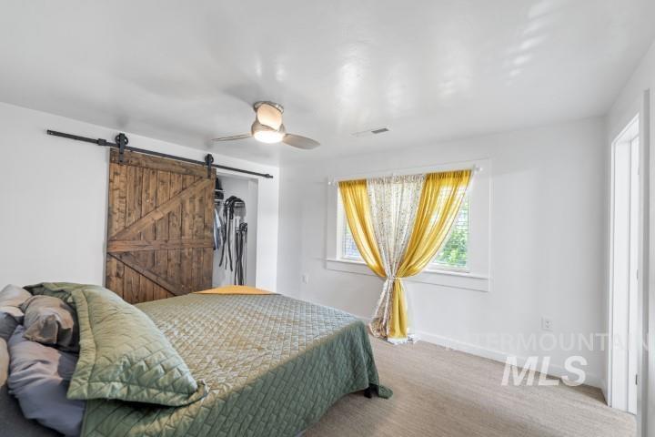Bedroom featuring ceiling fan, a barn door, a closet, and carpet