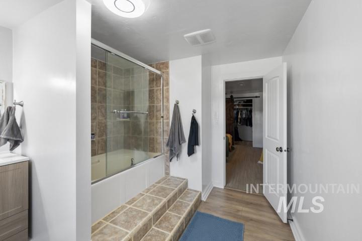 Full bathroom with light wood-type flooring, tiled shower / bath combo, vanity, and a spacious closet