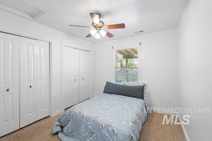 Bedroom featuring two closets, attic access, light carpet, and ceiling fan