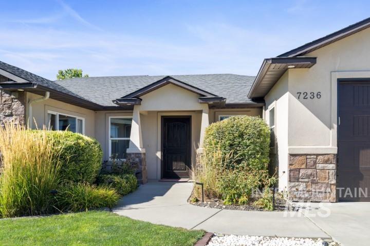 Doorway to property featuring a shingled roof, stucco siding, stone siding, and a garage