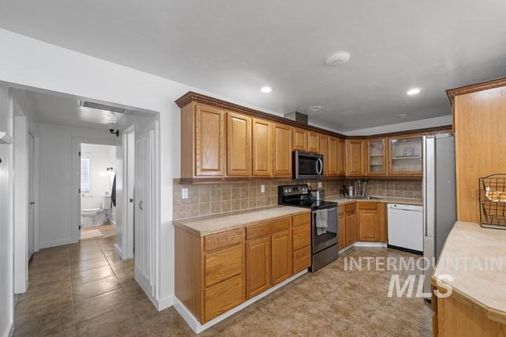 Kitchen with stainless steel appliances, light countertops, decorative backsplash, brown cabinets, and light tile patterned floors