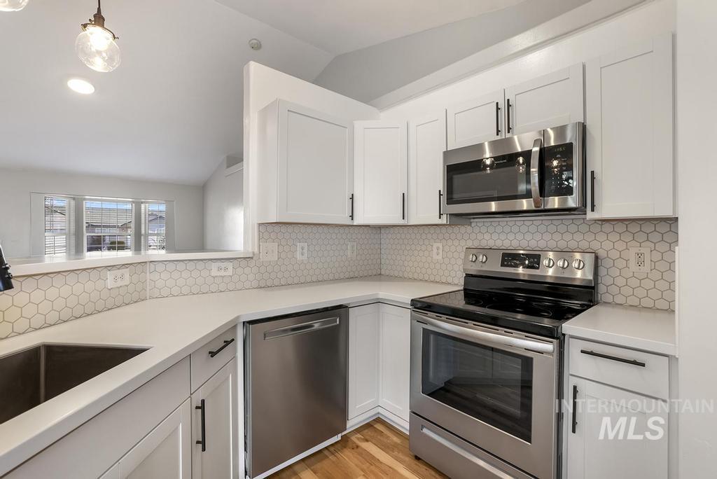 Kitchen featuring appliances with stainless steel finishes, lofted ceiling, white cabinetry, backsplash, and decorative light fixtures