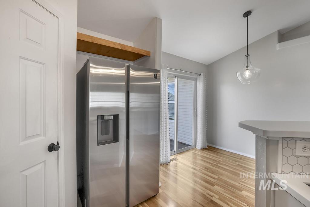 Kitchen featuring stainless steel refrigerator with ice dispenser, hanging light fixtures, light wood-type flooring, light countertops, and lofted ceiling