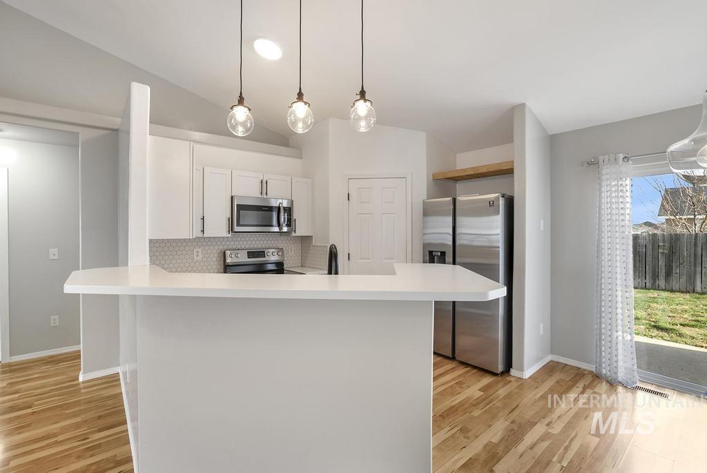 Kitchen with appliances with stainless steel finishes, light countertops, lofted ceiling, decorative light fixtures, and decorative backsplash
