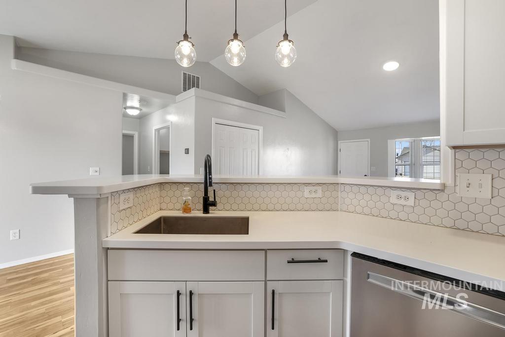 Kitchen featuring dishwasher, white cabinets, backsplash, lofted ceiling, and pendant lighting