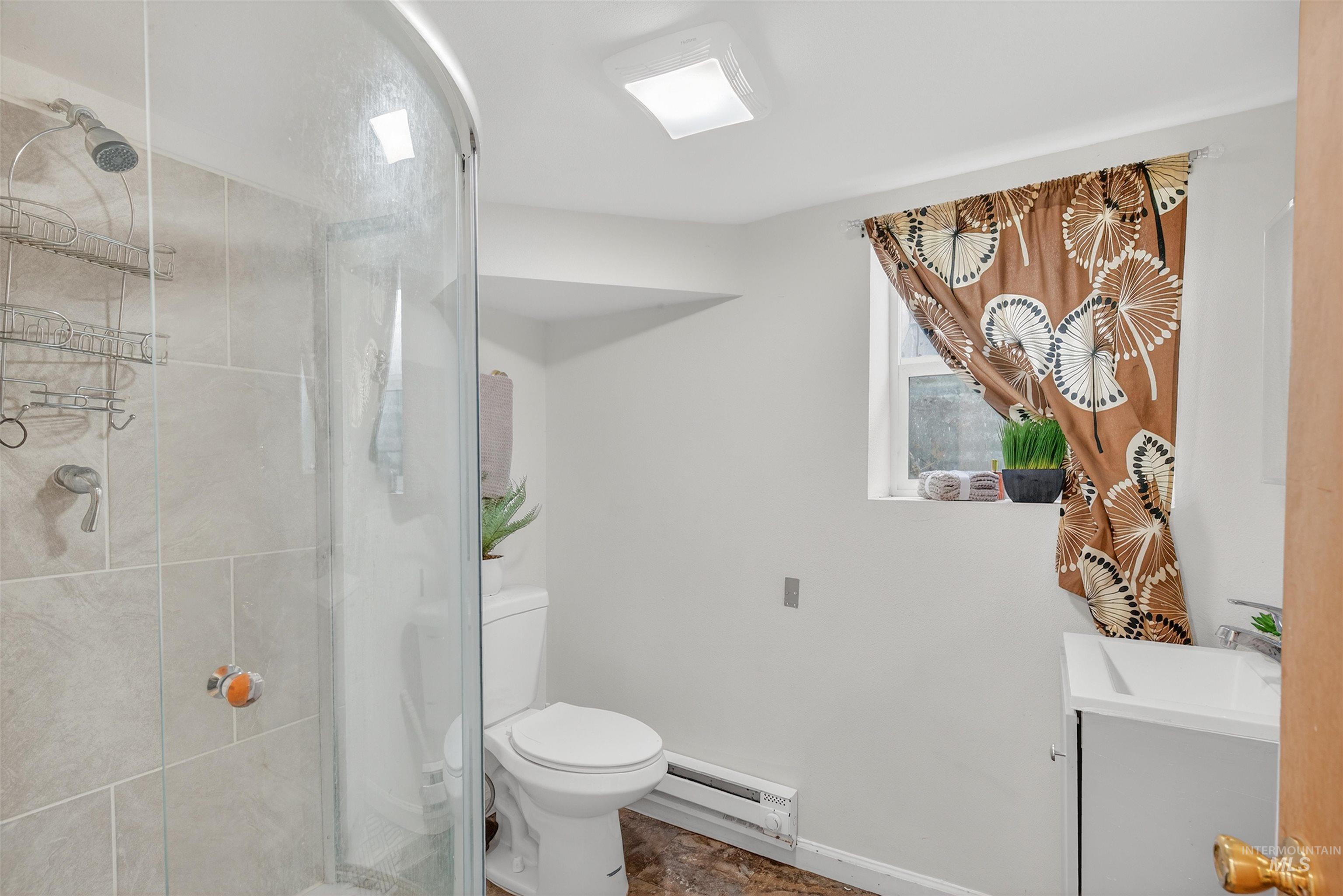Full bathroom with vanity, baseboard heating, and a shower stall