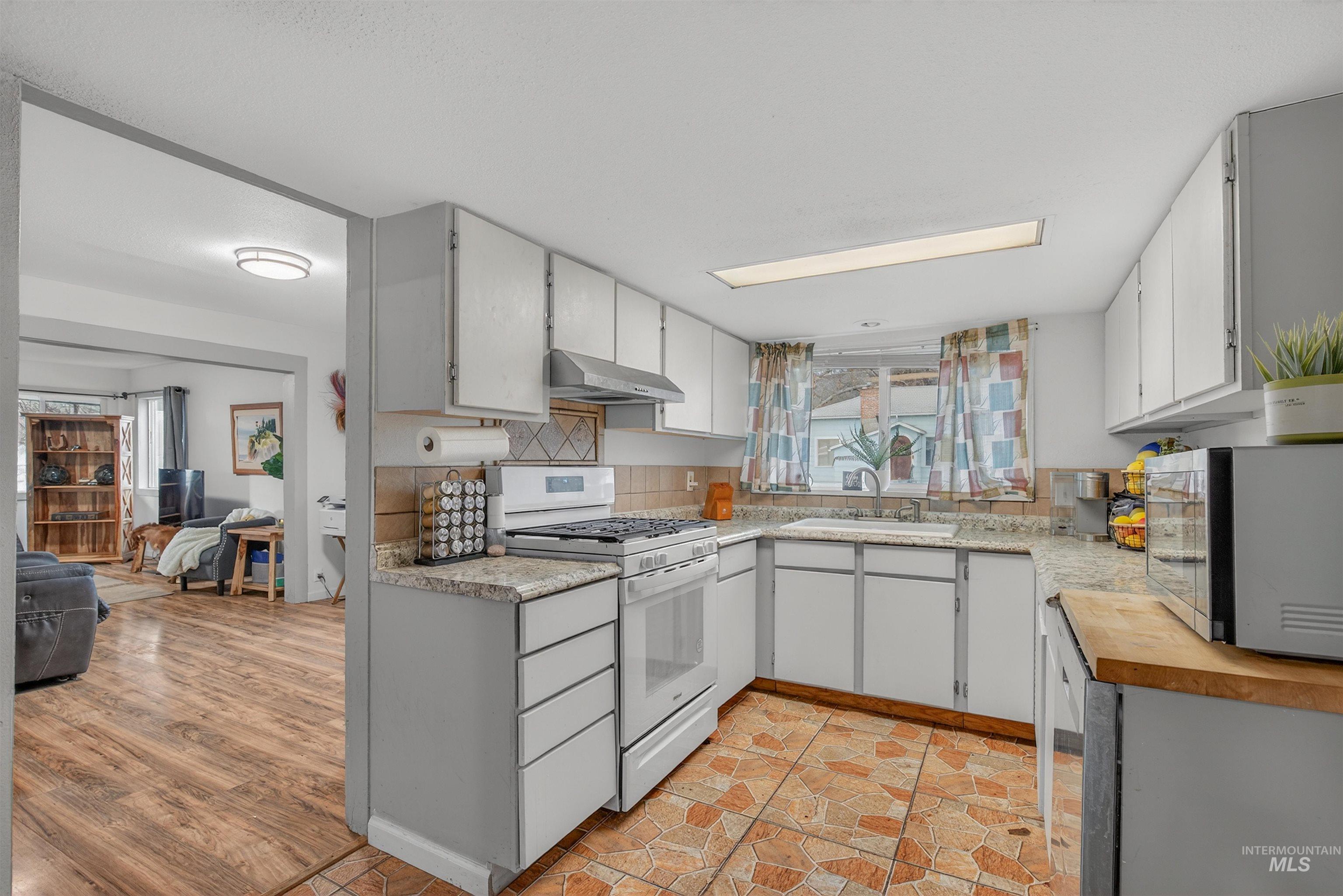 Kitchen with white gas range oven, stainless steel microwave, tasteful backsplash, butcher block counters, and under cabinet range hood