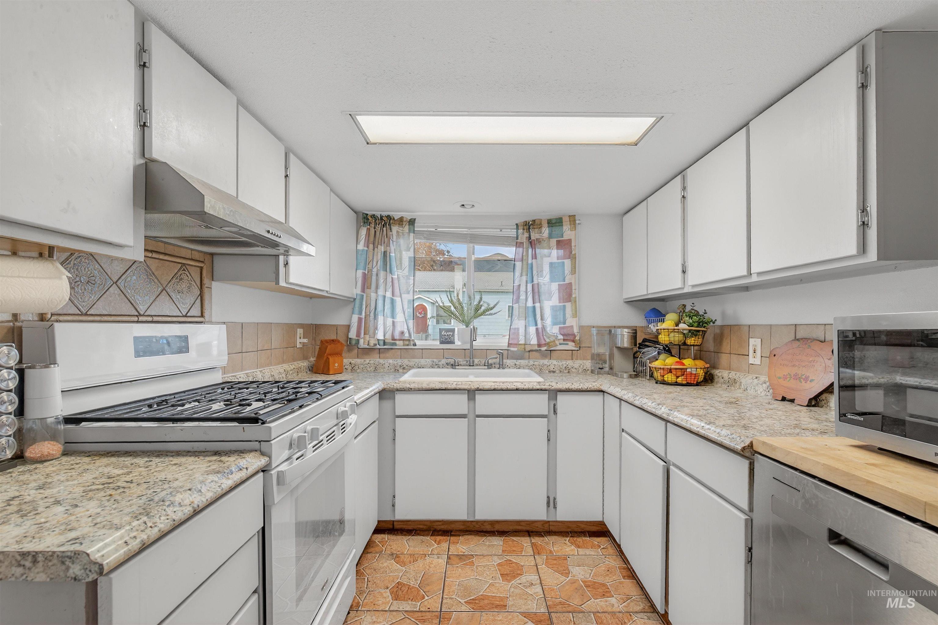 Kitchen with appliances with stainless steel finishes, backsplash, under cabinet range hood, and white cabinetry