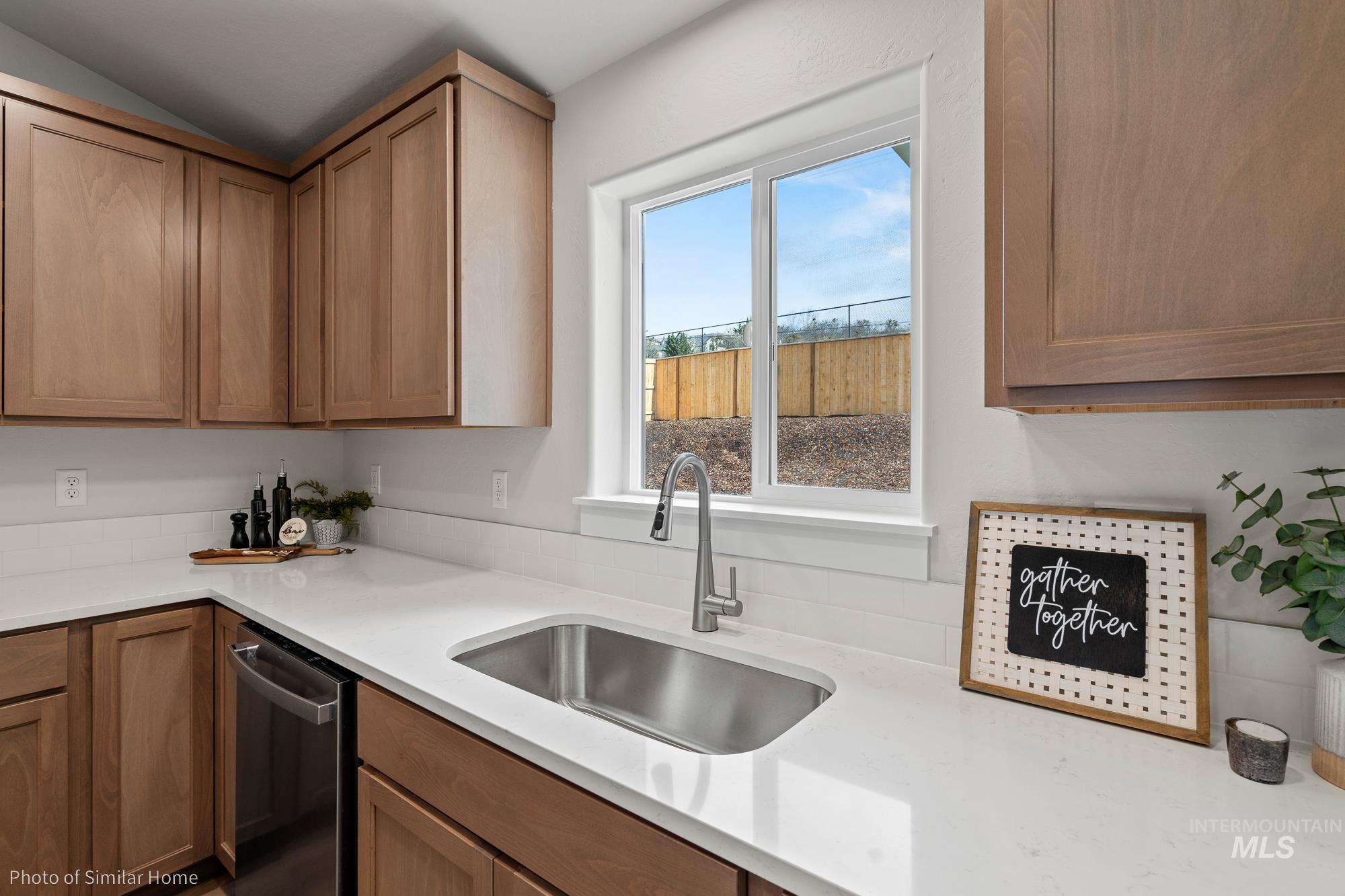 Kitchen featuring stainless steel dishwasher, light countertops, vaulted ceiling, and brown cabinets