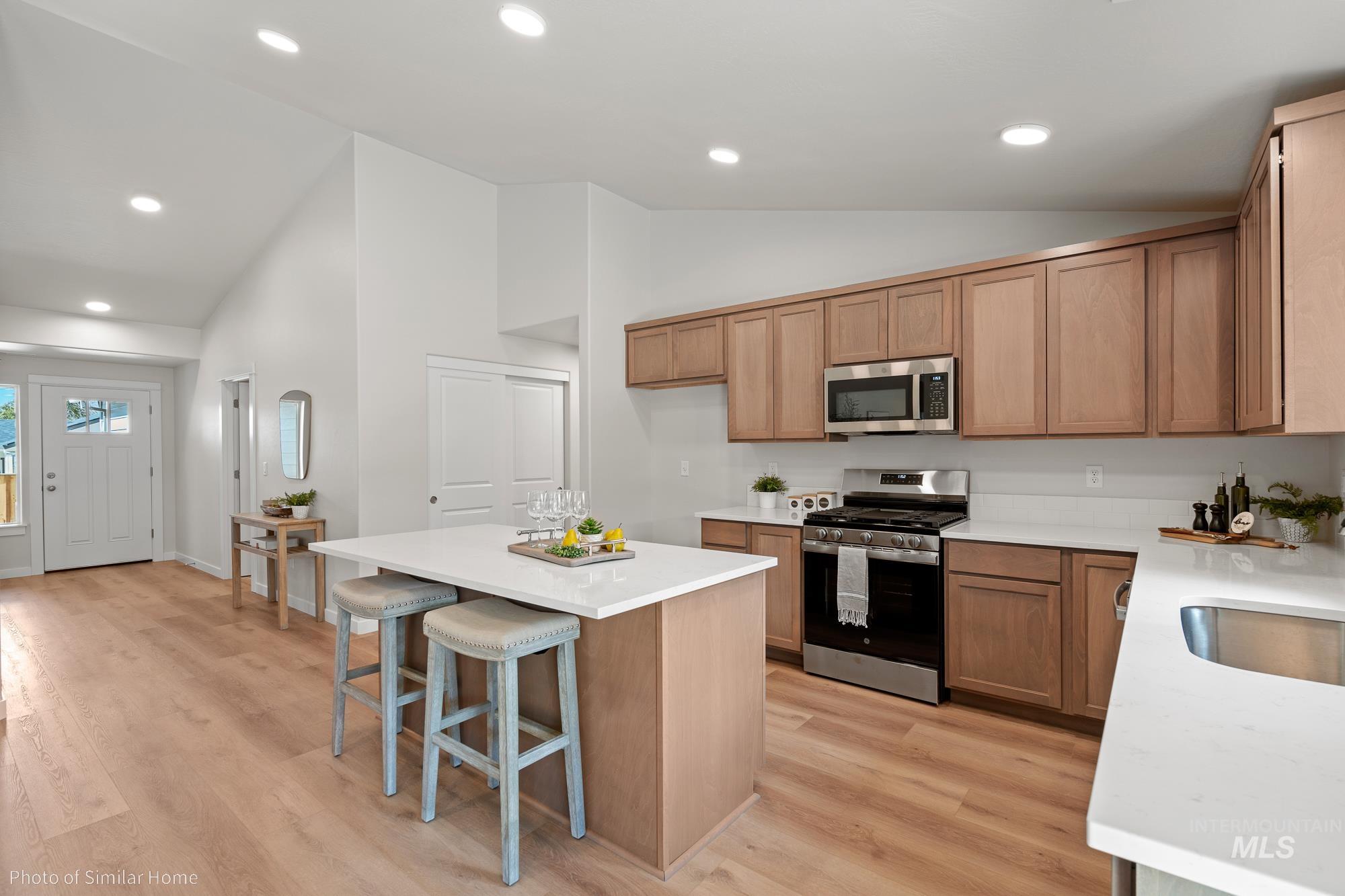 Kitchen with appliances with stainless steel finishes, a breakfast bar area, brown cabinets, light countertops, and recessed lighting