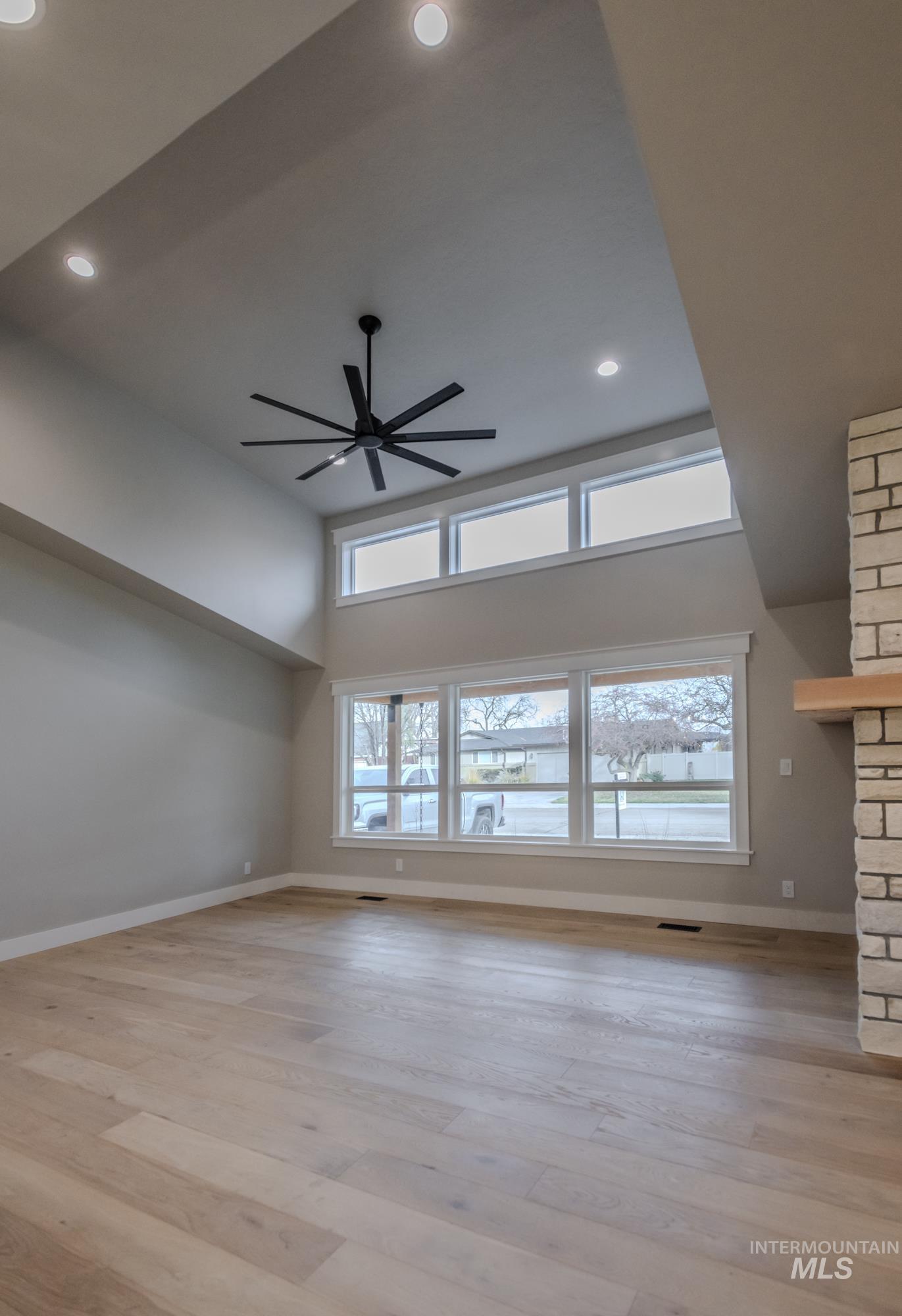 Living room featuring a towering ceiling, light wood flooring, recessed lighting, a ceiling fan, tons of natural light.