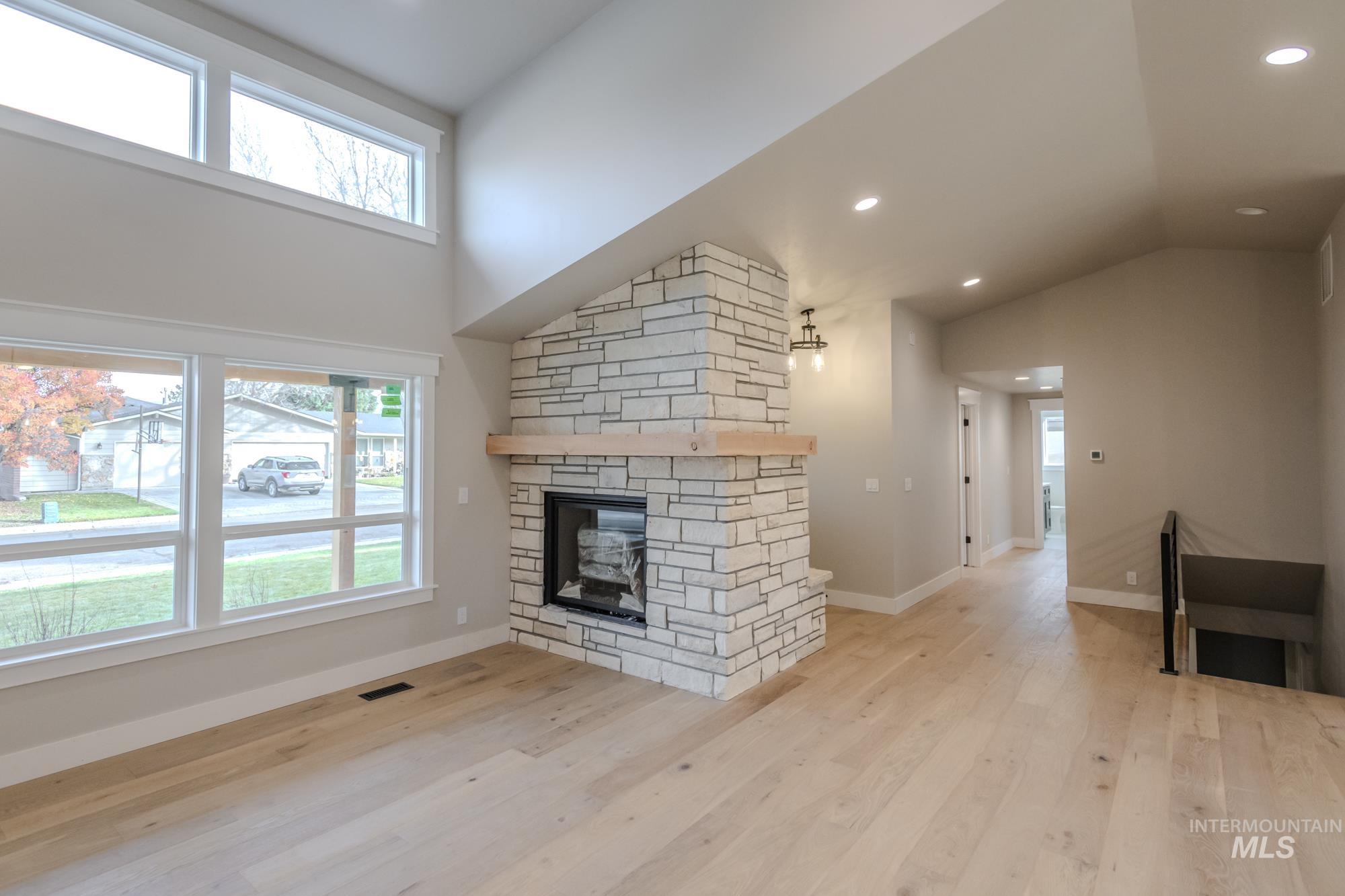 Living room with light wood flooring, a stone gas fireplace, high vaulted ceiling, dormer, lots of natural light, and recessed lighting