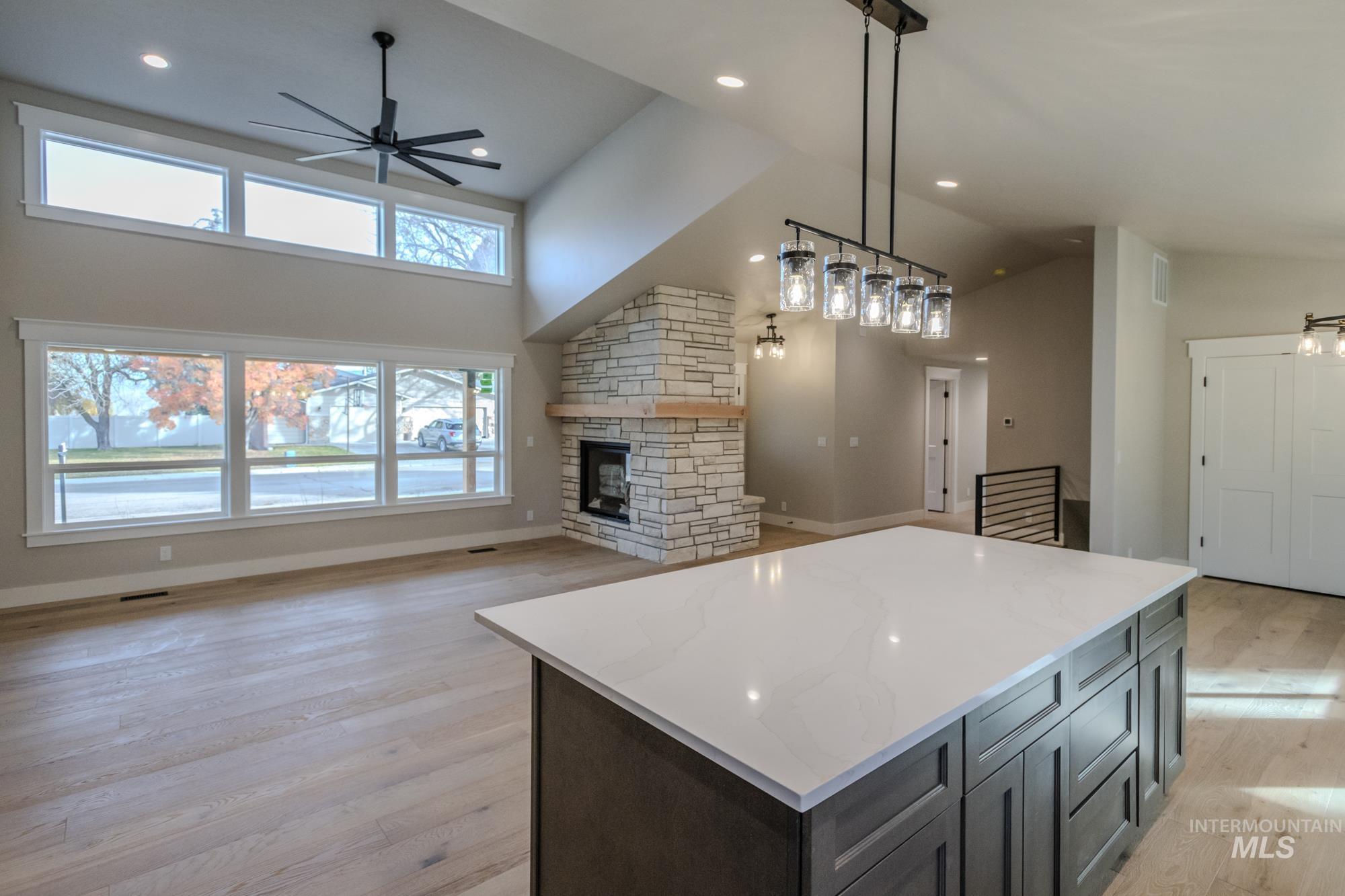 Kitchen with a gas stone fireplace, ceiling fan, light wood-style flooring, high vaulted ceiling, dormer, lots of natural light and open floor plan