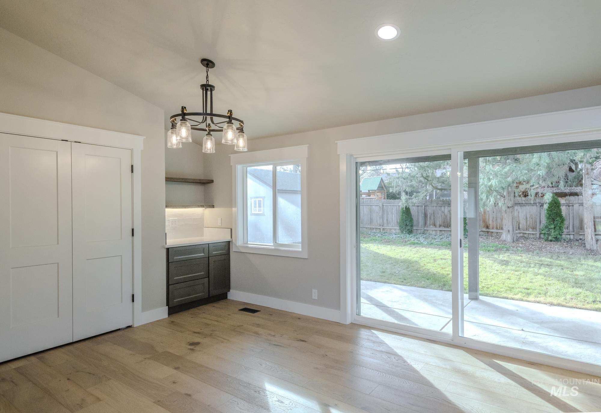 Dining area featuring light wood-type flooring, a chandelier, coffee bar with underlit floating shelves, and recessed lighting opening up through huge slider doors to ceder covered patio.