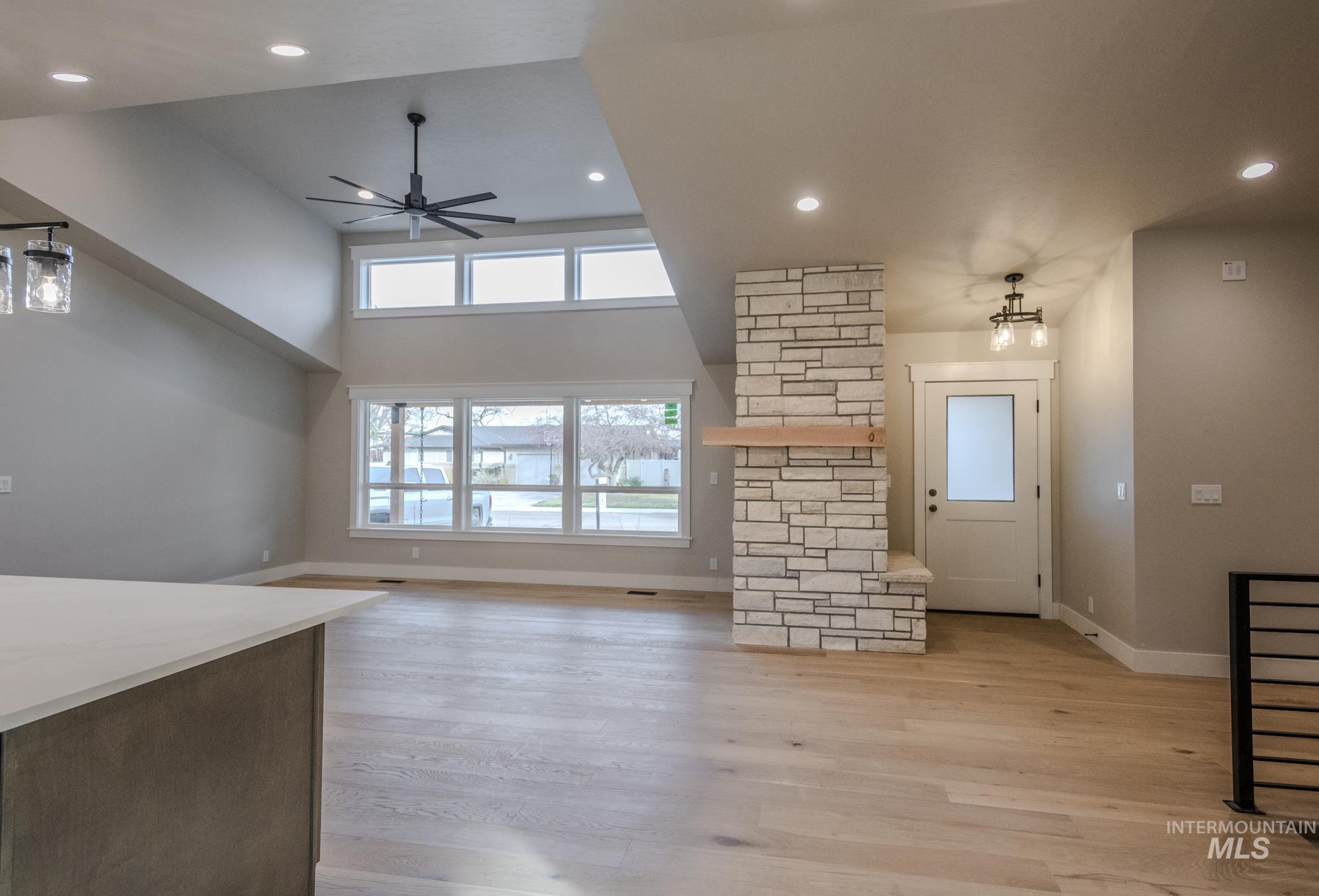 Living room and entry way with light wood floors, ceiling fan, a high ceiling, dormer, stone gas fireplace and recessed lighting