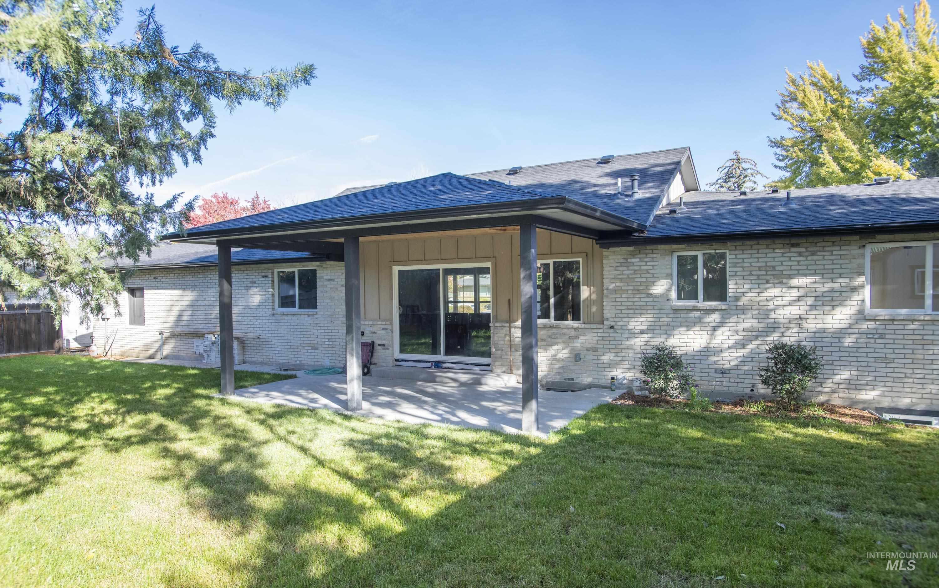 Back of house featuring a ceder covered patio area with circulating fan, brick siding, board and batten siding, and a shingled roof