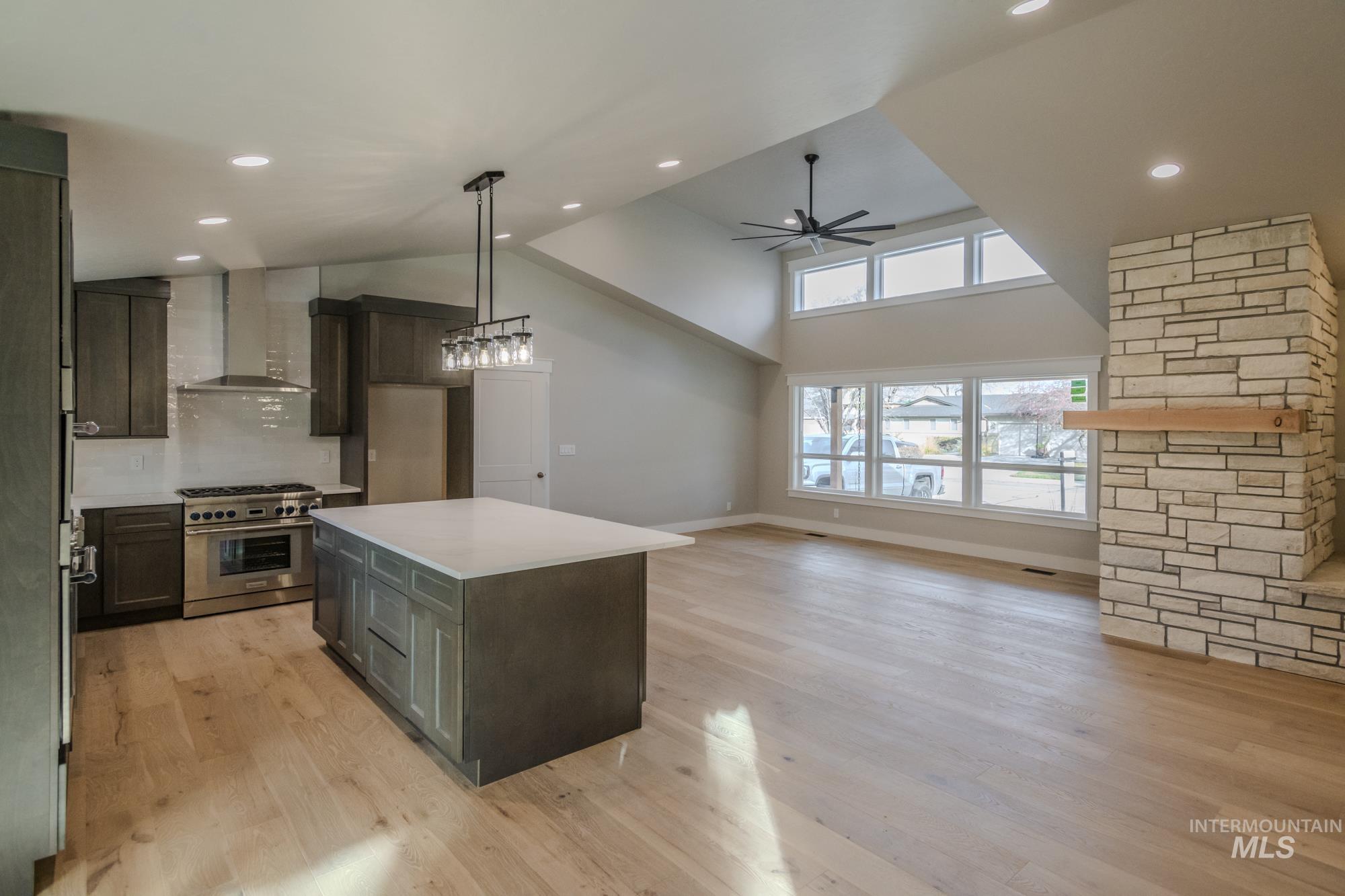 Kitchen with high end range, a kitchen island, ceiling fan, high vaulted ceiling, lots of natural light, wall chimney exhaust hood, and full stone gas fireplace.