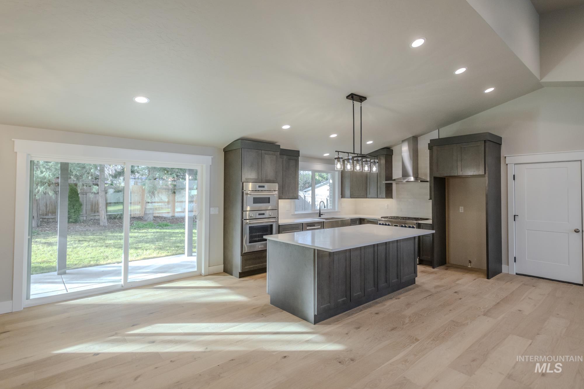 Kitchen featuring a kitchen island, vaulted ceiling, decorative light fixtures, wall chimney exhaust hood, and stainless steel Thermador double oven, with oversized slider to huge ceder covered back patio.