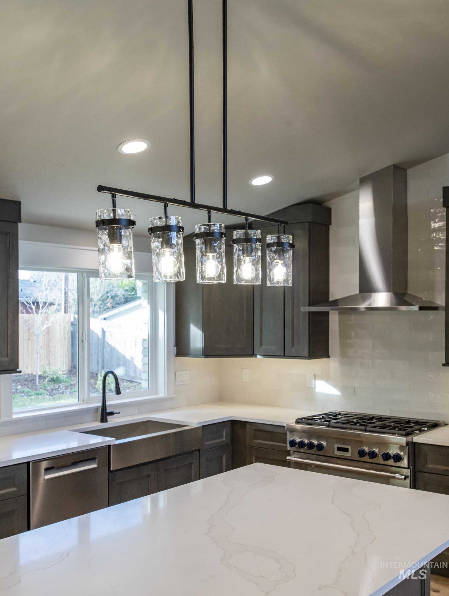Very light and bright Kitchen featuring wall chimney exhaust hood, stainless steel Thermador appliances, dual ovens, gas range, decorative backsplash, quartz counters, huge island and hanging light fixtures