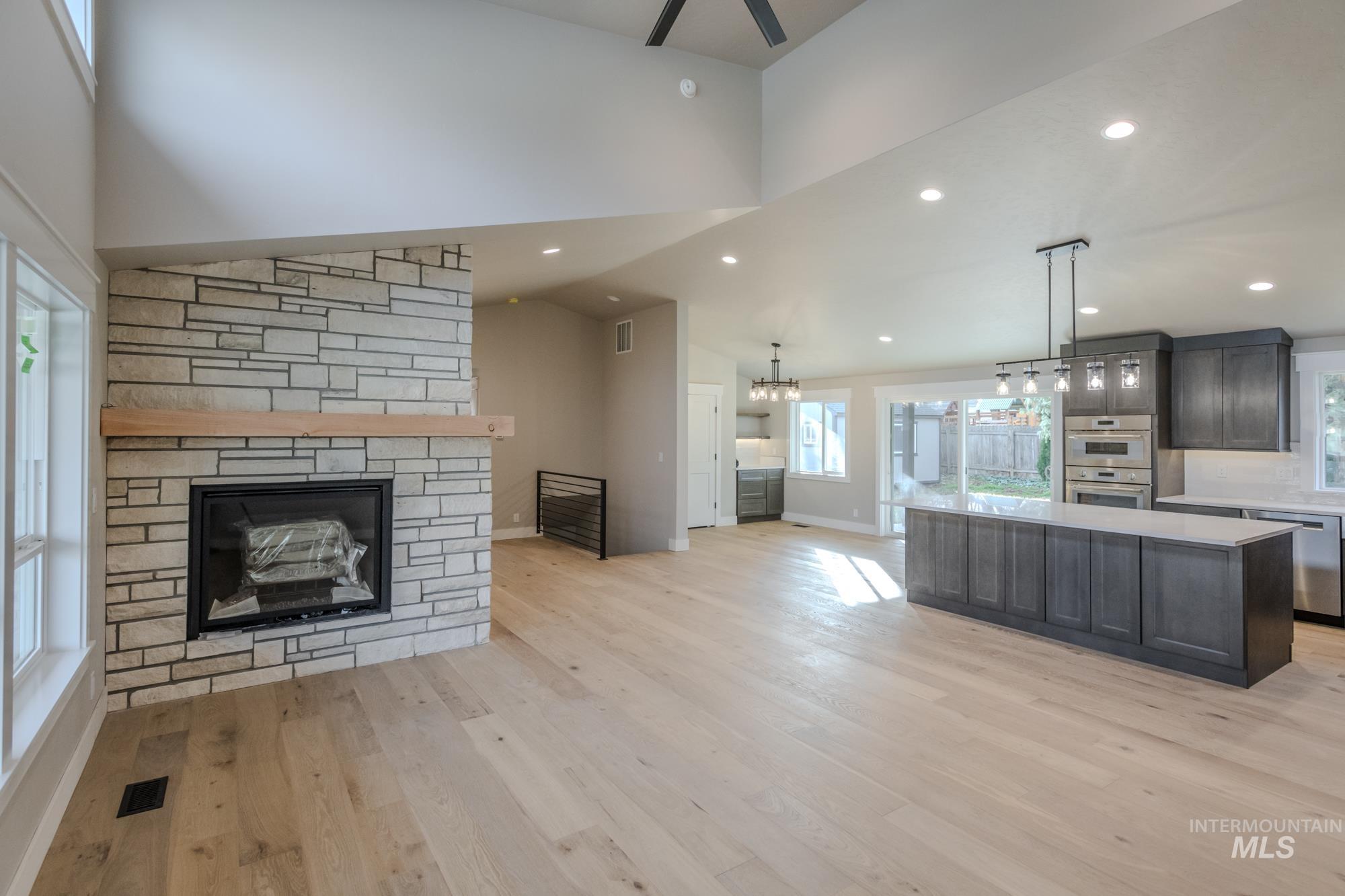 Main level living room featuring a stone gas fireplace, light wood-style flooring, recessed lighting, a ceiling fan, and high vaulted ceiling with dormer.