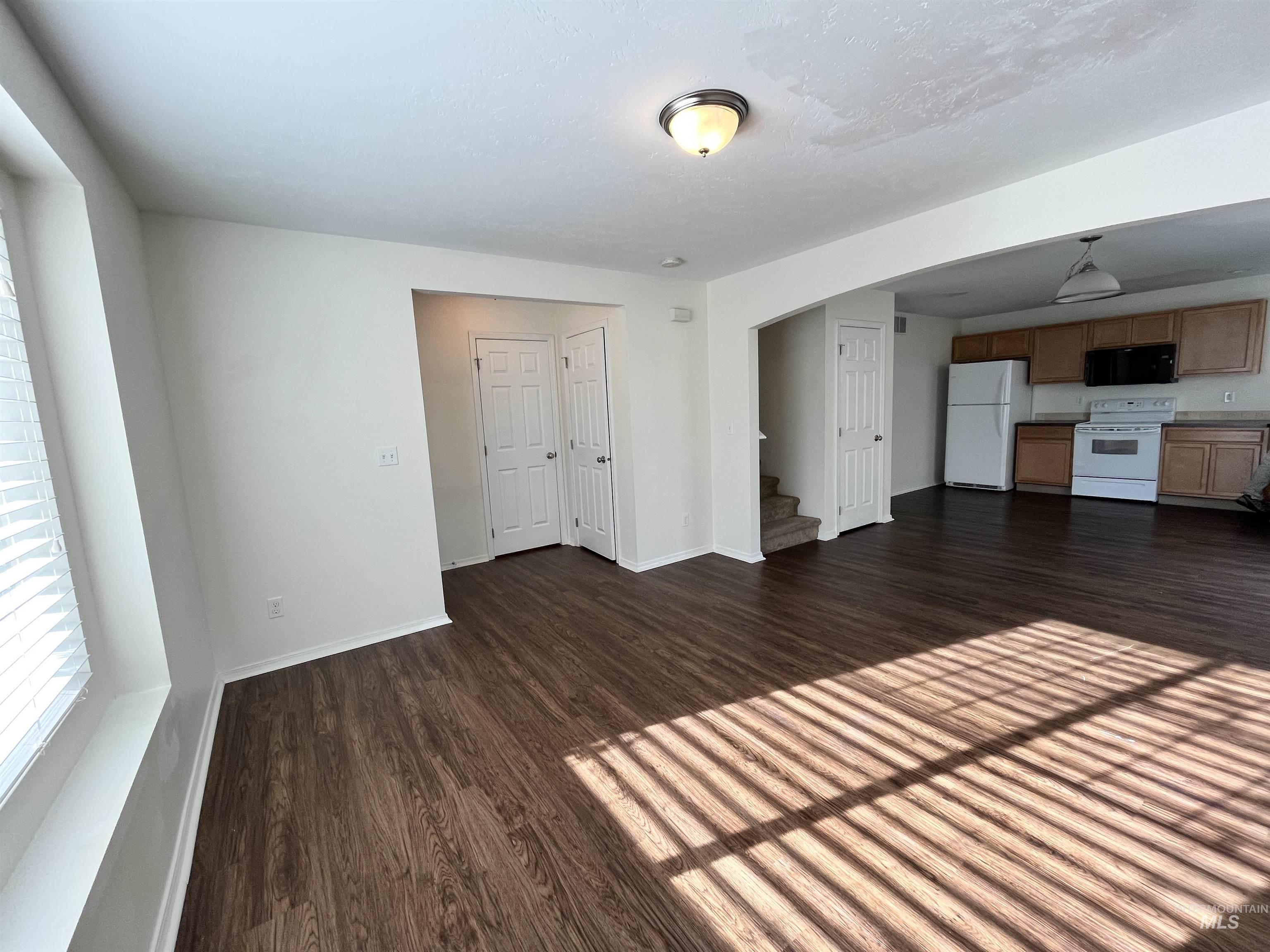 Unfurnished living room with dark wood-style flooring, stairs, and arched walkways