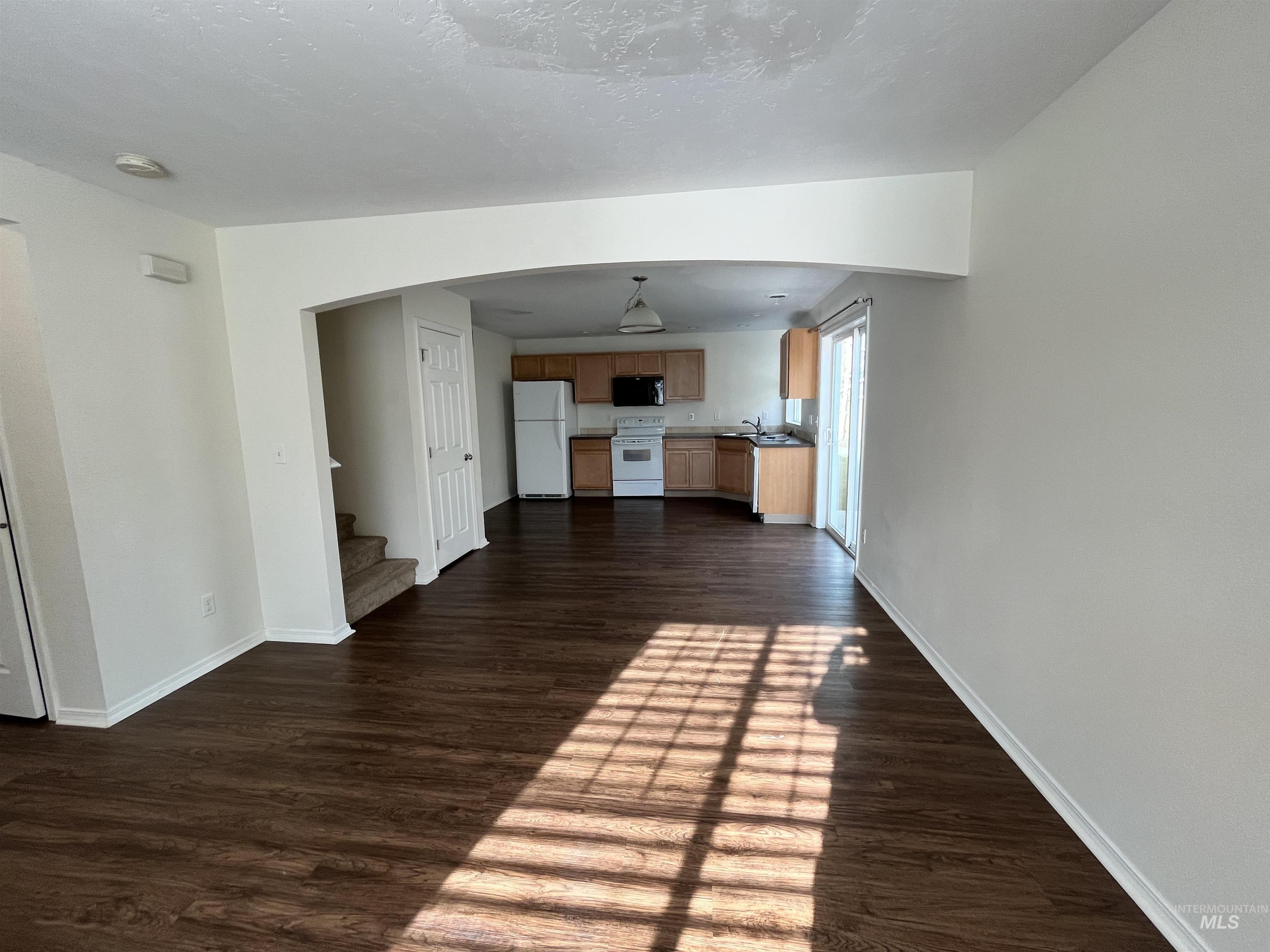 Unfurnished living room featuring dark wood finished floors, stairs, arched walkways, and a textured ceiling