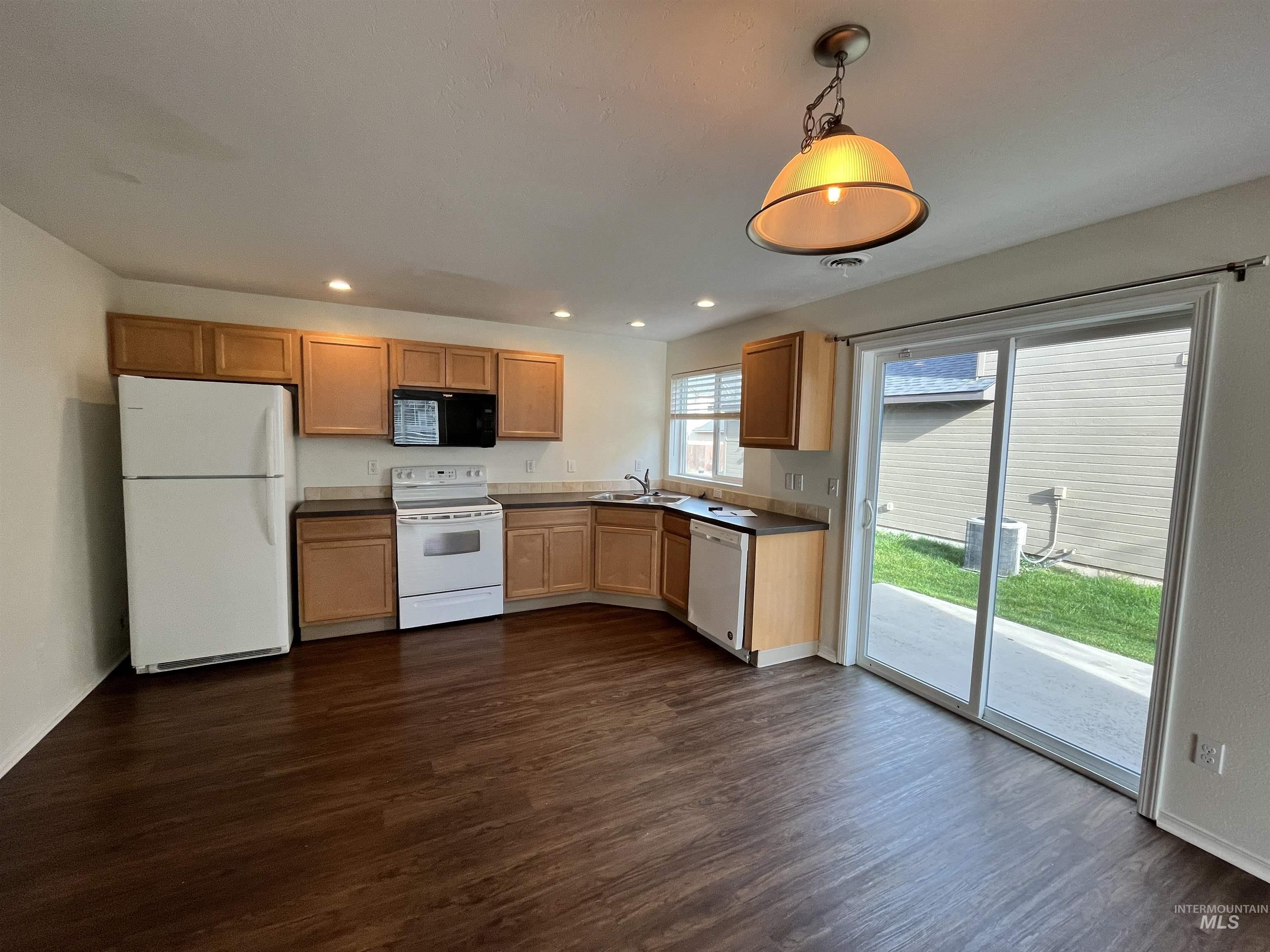 Kitchen featuring white appliances, dark countertops, hanging light fixtures, recessed lighting, and dark wood-style flooring