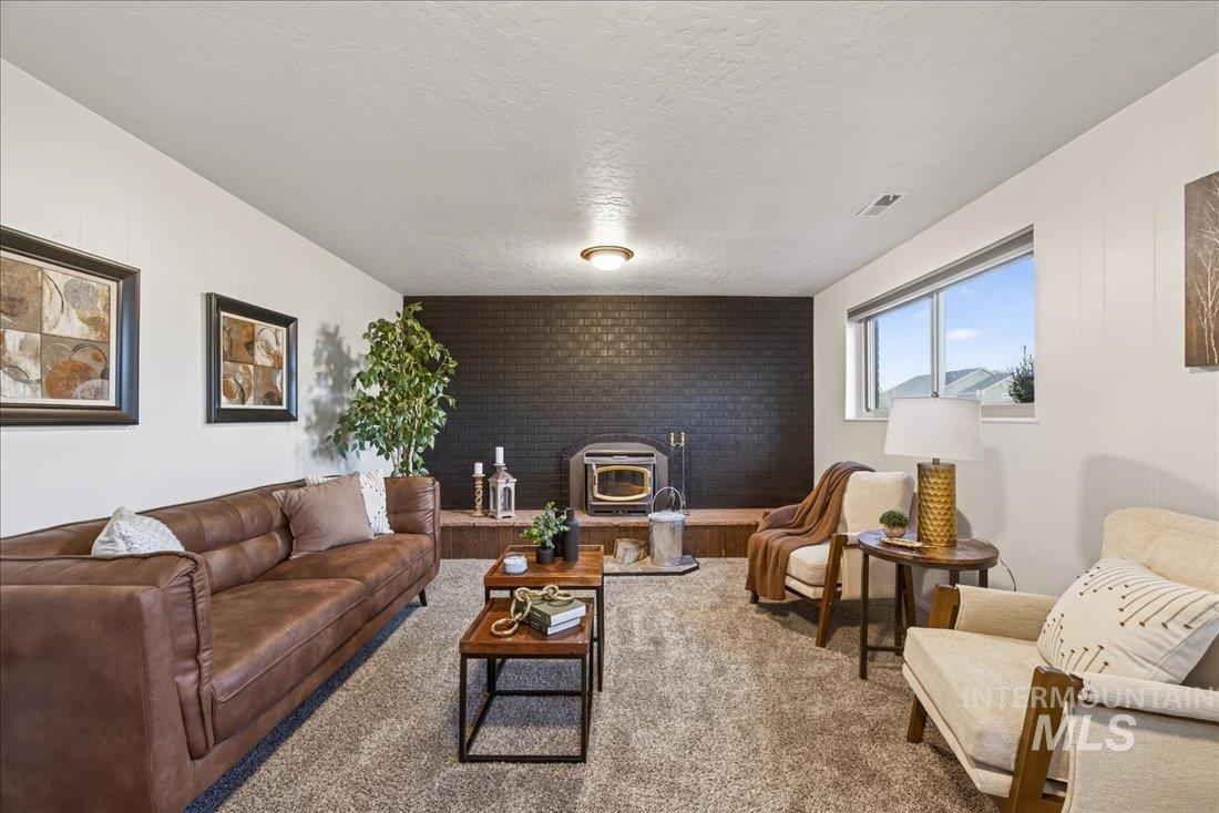 Carpeted living area featuring a wood stove, a textured ceiling, brick wall, and an accent wall
