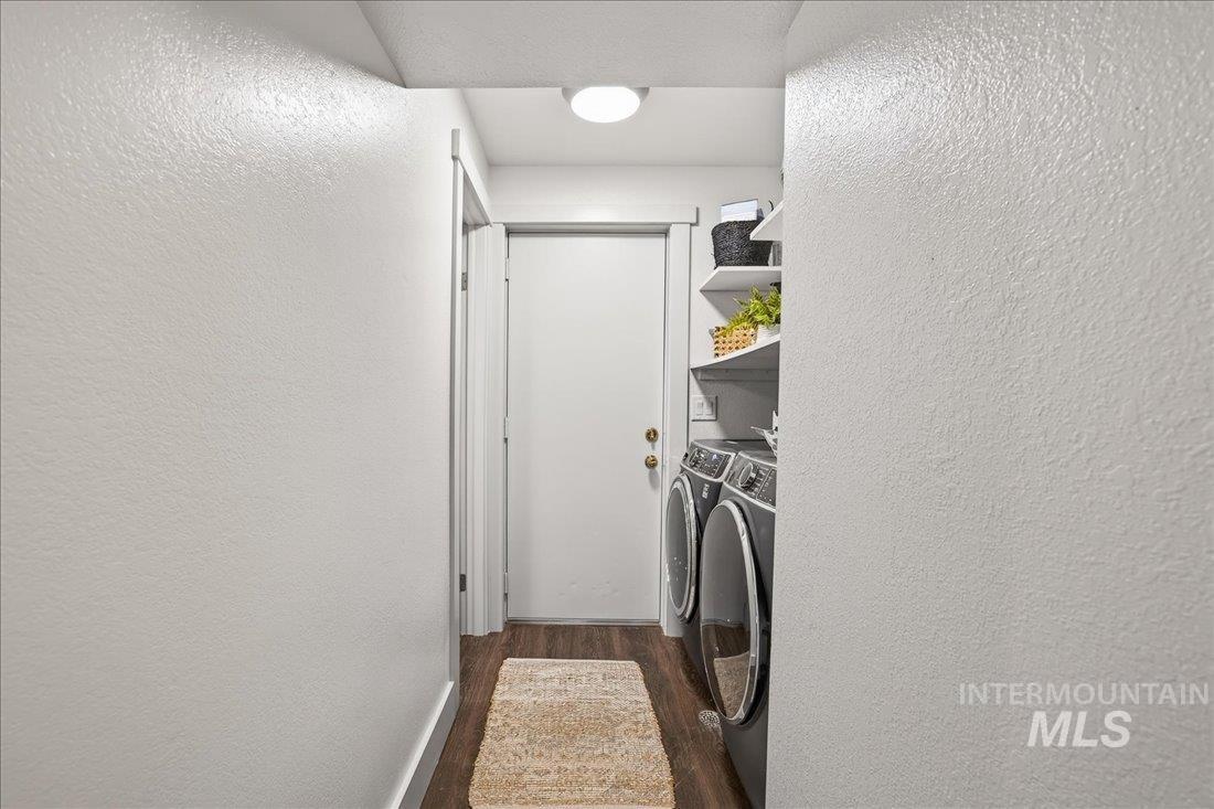 Laundry area featuring a textured wall, washing machine and clothes dryer, and dark wood-type flooring